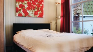 Een keurig opgemaakt bed met een witte spreideken, een zwart hoofdbord en een bloemschilderij boven de muur.