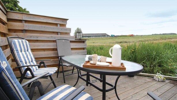 Een houten terras met een glazen tafel en gestreepte stoelen, met uitzicht op een grasveld.