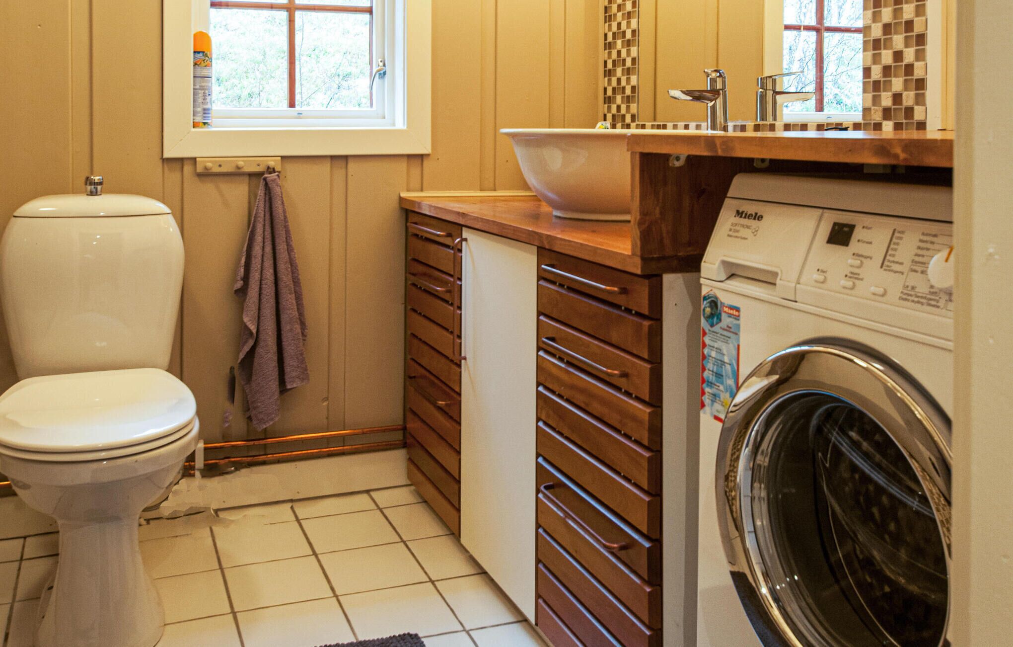 A compact bathroom with a toilet, a washing machine, and a sink with a wooden countertop.