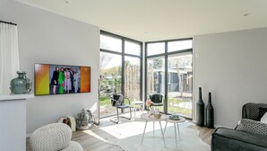 Una sala de estar moderna con un amplio ventanal que da a un espacio al aire libre, un televisor montado en la pared y un rincón de estar acogedor.