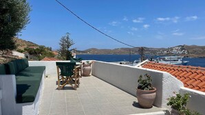 A terrace with a green sofa, wooden chair, and potted plants. - Charming two Bedroom Fisherman's House on Kea (Kea)