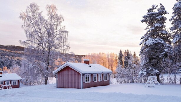 A small, single-story cabin with a red exterior and white trim, surrounded by snow-covered trees and a forested landscape. - Amazing Home in Sysslebäck With 2 Bedrooms and Wifi (Sysslebäck)