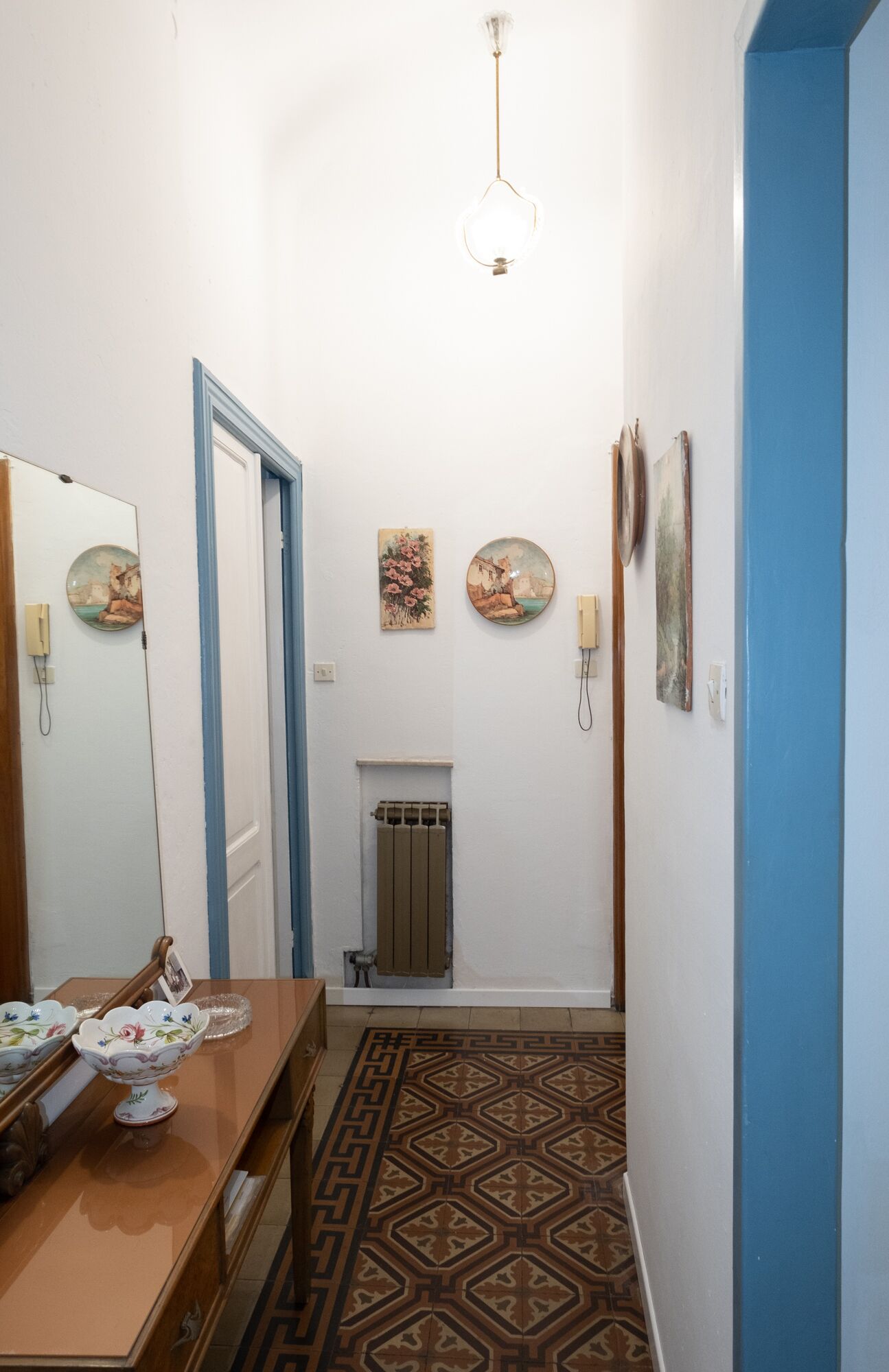 Un couloir avec une porte bleue, un radiateur et un sol à motifs.