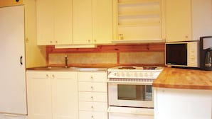 Eine kleine Küche mit weißen Schränken, einem Herd, einem Backofen, einer Mikrowelle und einer Holz Arbeitsplatte.