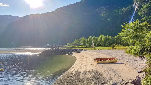 En strand med en båt på sanden, en klar himmel och ett berg i bakgrunden.