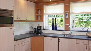 Une cuisine moderne avec des meubles en bois, un four encastré, une machine à café et une fenêtre avec des rideaux.