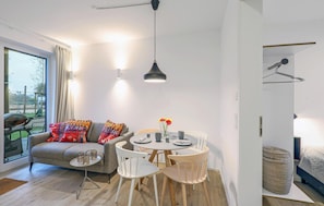 A modern living room with a grey sofa, colorful throw pillows, a round dining table with white chairs, and a hanging pendant light. - Amazing Apartment in Lembruch/dümmer See With 2 Bedrooms, Wifi and Indoor Swimming Pool (Lembruch)