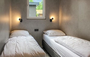 A small, compact room with two single beds, a window, and wall-mounted lights.