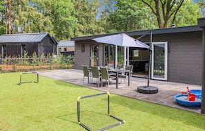 A modern outdoor patio with a dining table and chairs, a covered seating area, and a play area with a sandpit and toys.