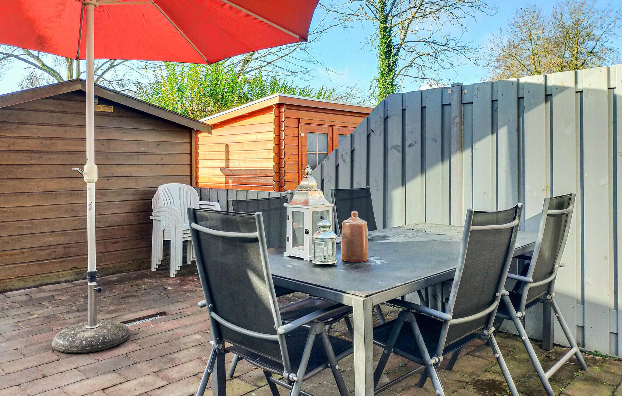 An outdoor patio with a table and chairs, a red umbrella, a lantern, and a small shed in the background.