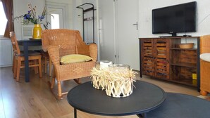 A living room with a wicker chair, a round black table, and a TV on a wooden cabinet.