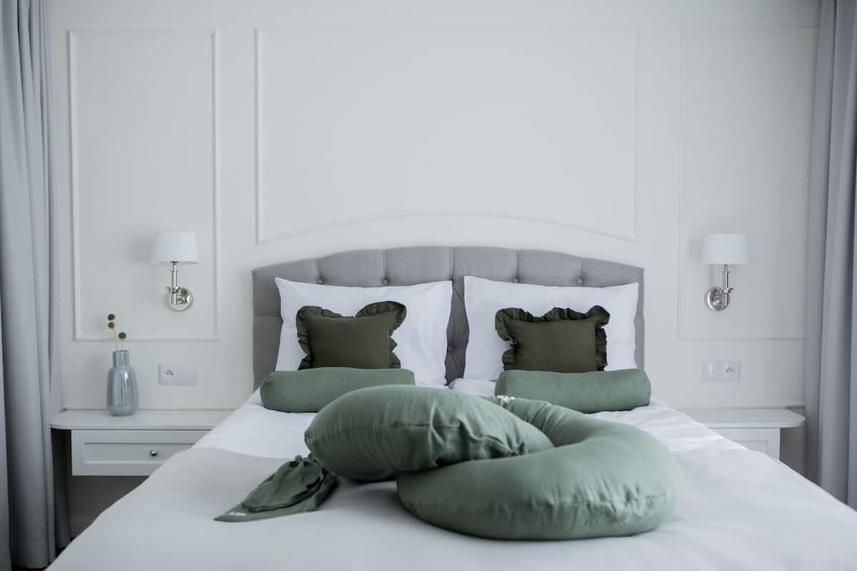 A neatly made bed with a grey headboard, two bedside tables with lamps, and a vase with flowers on the left side.