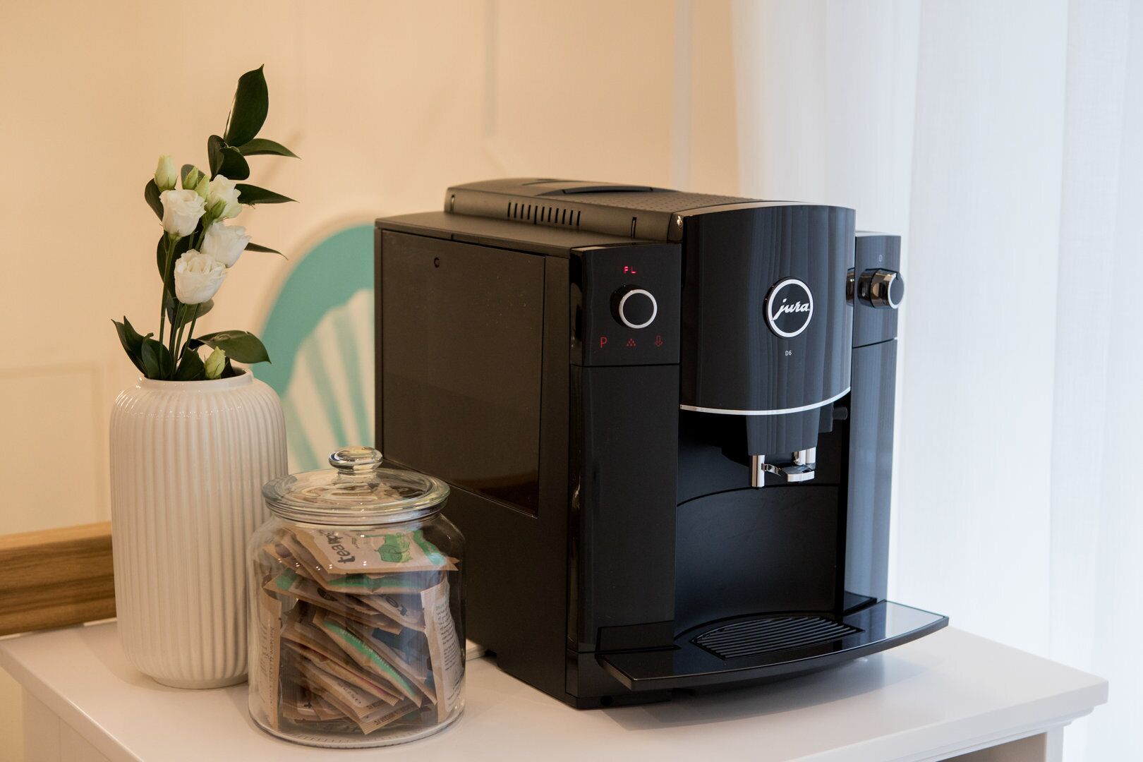 A black coffee machine with a water reservoir and a jar of tea bags on a white table.