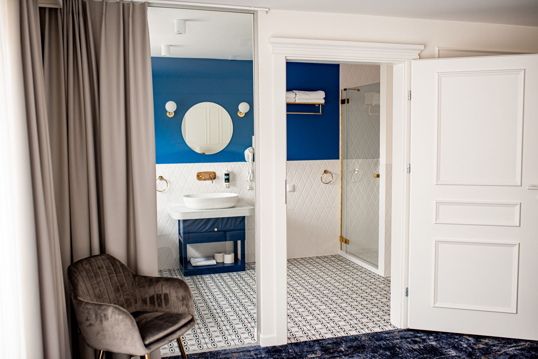 Habitación de hotel con baño que presenta una pared de acento azul, un lavamanos blanco, un espejo y una zona de ducha.