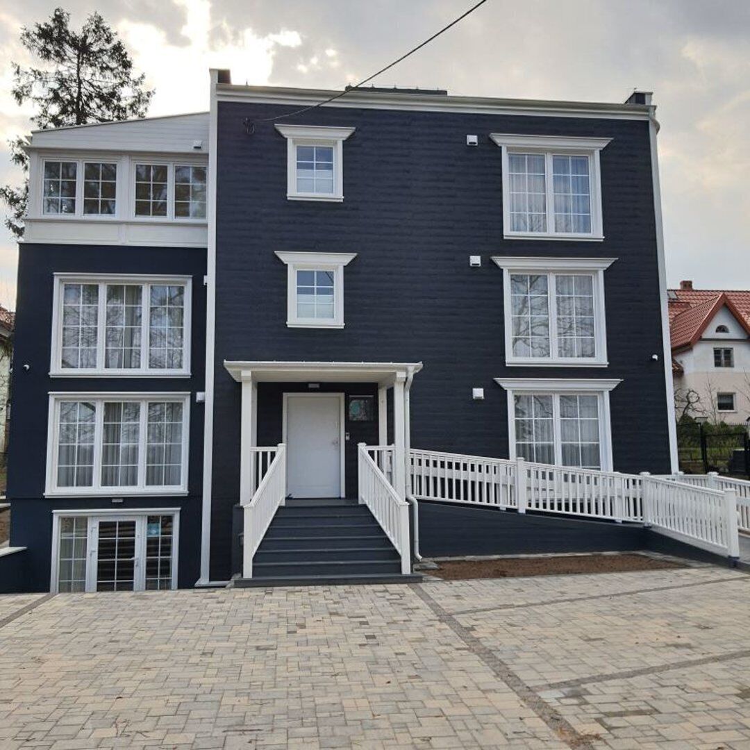 Un edificio de varios pisos con fachada oscura, detalles blancos y una entrada principal con escaleras.