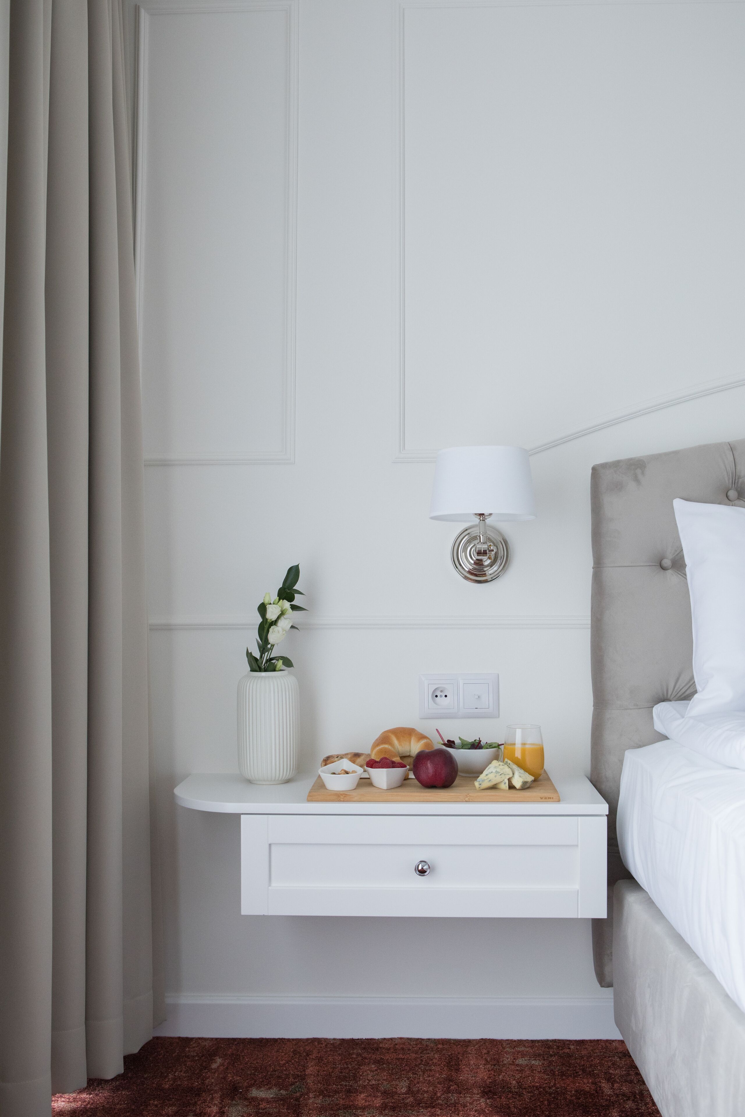 Une chambre d’hôtel bien rangée, avec un lit, une table de chevet dotée d’une lampe et une petite plante.