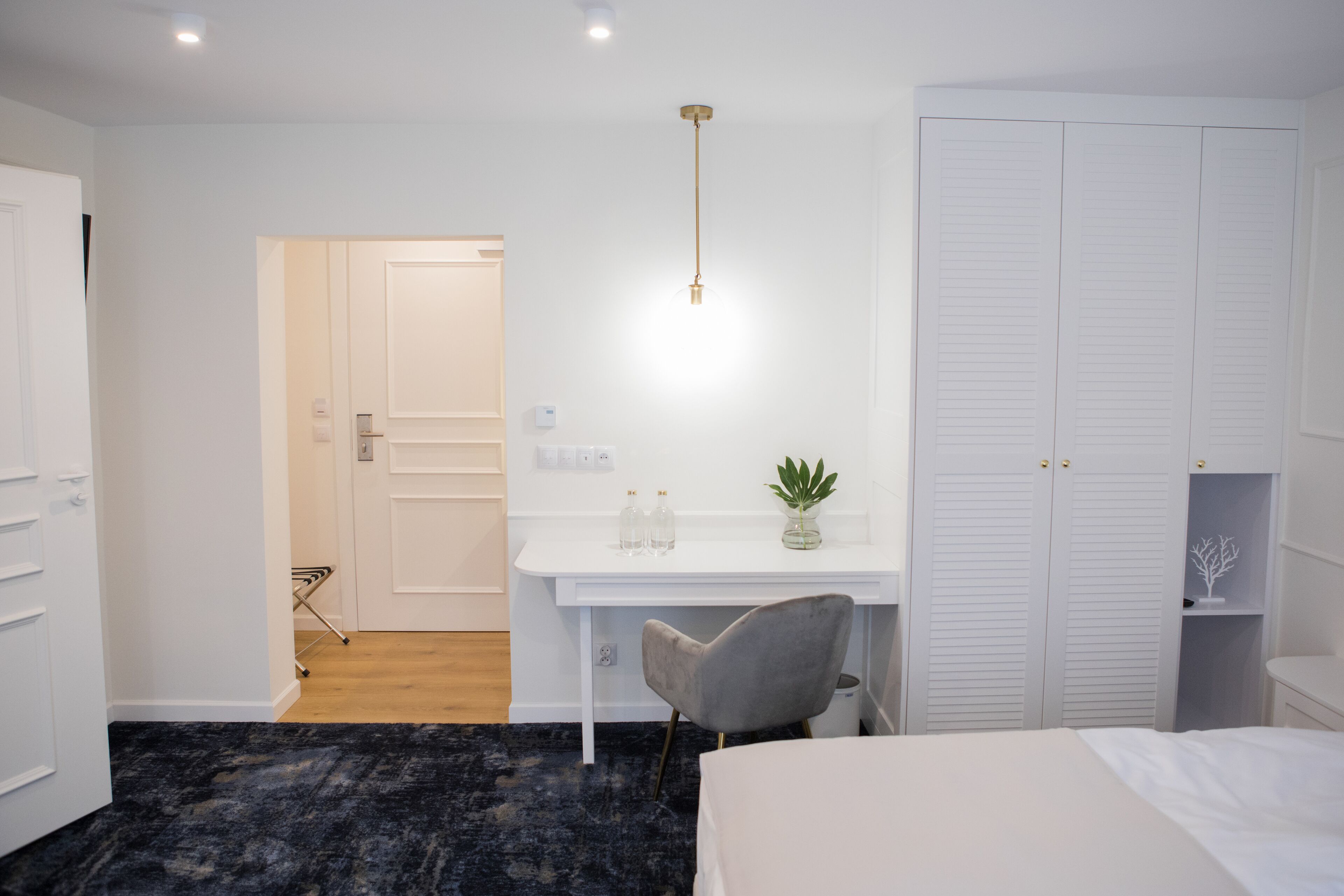 A bedroom with a bed, a desk, a chair, a wardrobe, and a plant.
