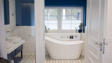 A modern bathroom with a freestanding bathtub, a vanity with two sinks, and a window with blinds.
