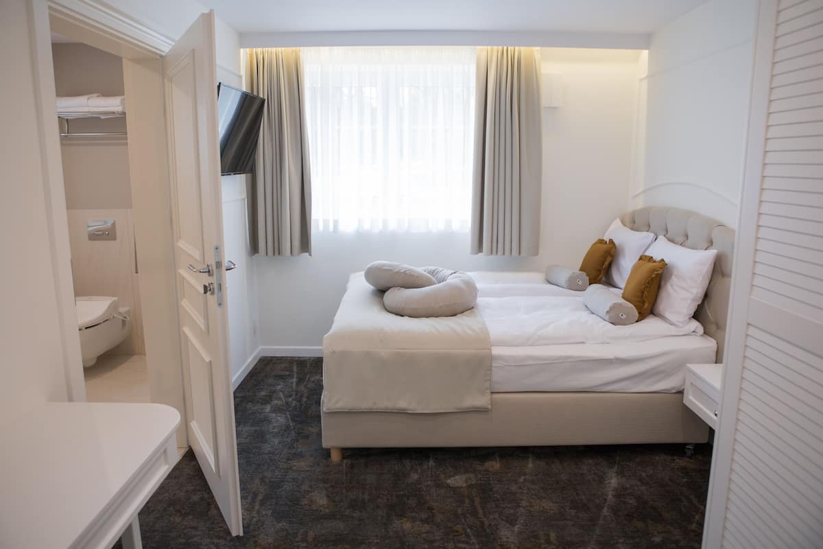 A hotel room with a bed, a TV mounted on the wall, a window with curtains, and a closet with a toilet.