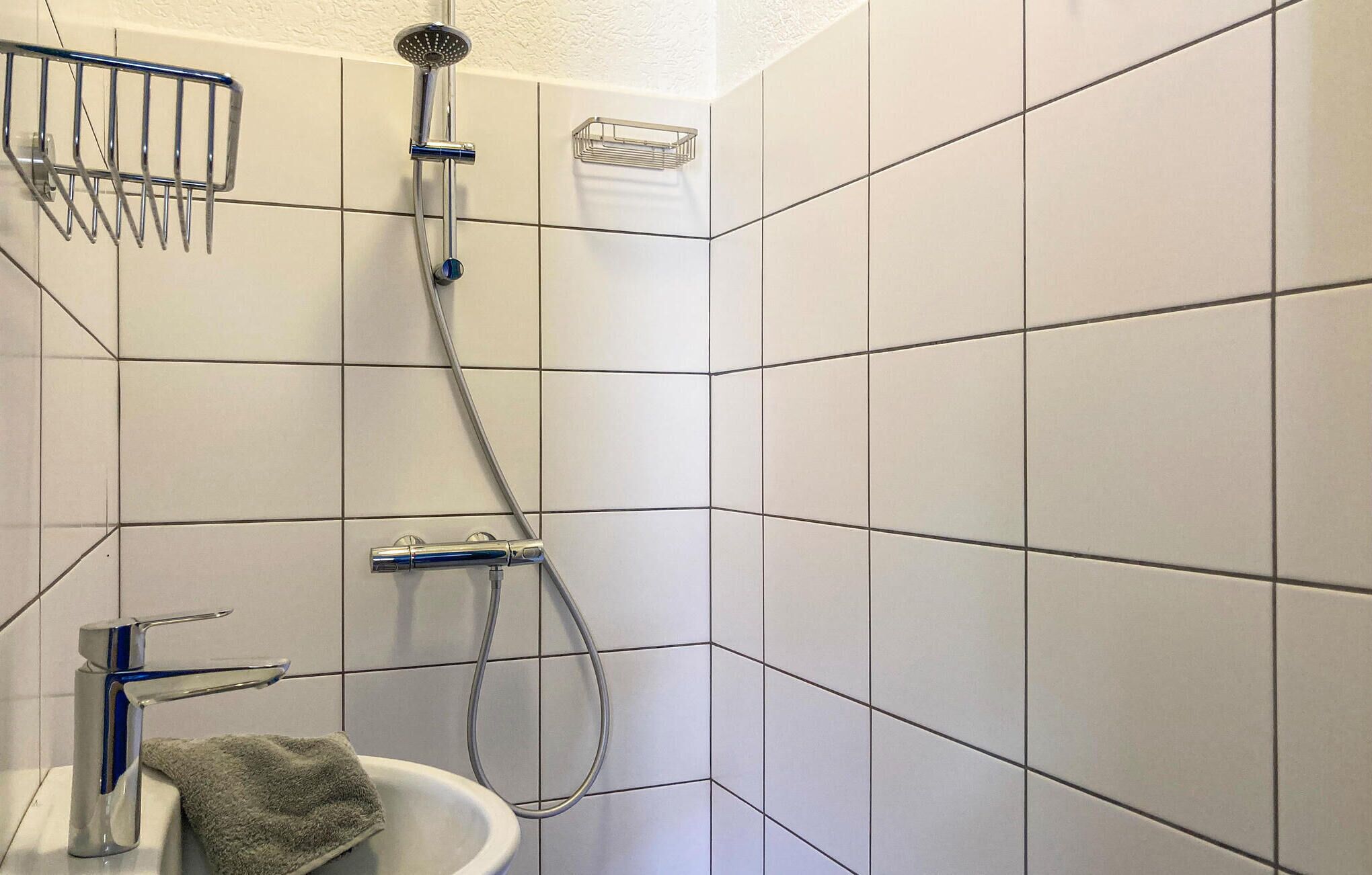 A bathroom with white tiled walls, a shower with a handheld showerhead, a sink with a faucet, and a towel hanging on the wall.