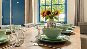 Una mesa de comedor dispuesta con platos, cuencos y cubiertos verdes, con un florero de girasoles en el alféizar de la ventana.
