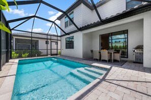 Ein Schwimmbad mit Terrassenbereich, Gartenmöbeln und Grill.