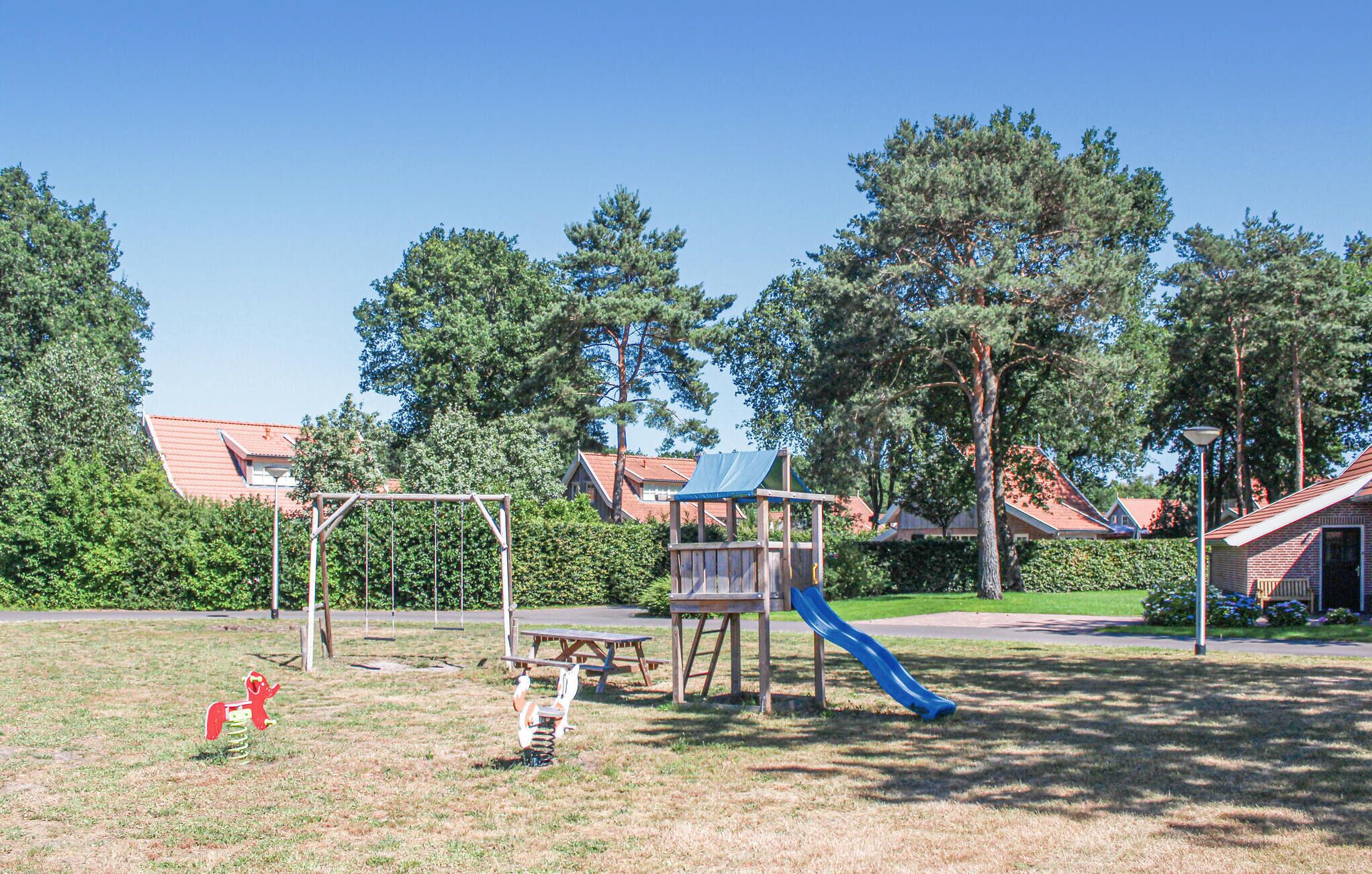 A playground with swings, a slide, and picnic tables in a park with houses and trees in the background.