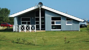 A single-story building with a gabled roof, large windows, and a white porch with a railing. - Strandblick 1 (Brodersby)
