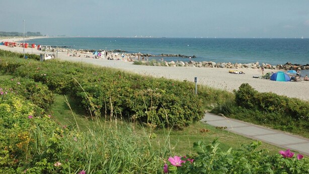 A beach with tents, a path, and a rocky shoreline. - Strandblick 1 (Brodersby)