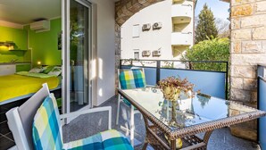 A balcony with a glass table, wicker chairs, and a view of a pool and buildings. - Stunning Apartment in Medulin With Wifi (Medulin)