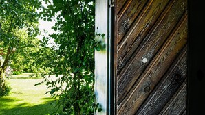 A wooden door with a metal handle, partially obscured by green foliage. - Nice Home in Lidköping With 2 Bedrooms, Sauna and Wifi (Lidköping)