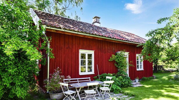 A red wooden house with a tiled roof, a garden with a bench and chairs, and a clear blue sky. - Nice Home in Lidköping With 2 Bedrooms, Sauna and Wifi (Lidköping)