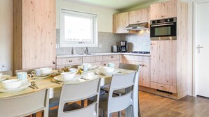 A modern kitchen with wooden cabinets, a built-in oven, and a dining area with white chairs and a table set for two. - Awesome Home in Heinkenszand With Wifi, 4 Bedrooms and Outdoor Swimming Pool (Heinkenszand)