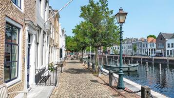 Een geplaveid pad langs een gracht, met traditionele gebouwen, banken en een lantaarnpaal.