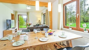 A dining area with a wooden table set for four, a sofa, and a television in the background. - Awesome Home in Kirchheim With 4 Bedrooms, Sauna and Wifi (Kirchheim)
