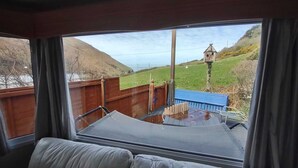 Una habitación con un gran ventanal que ofrece vistas a un paisaje rural, incluyendo una valla de madera y una estructura pequeña tipo torre.