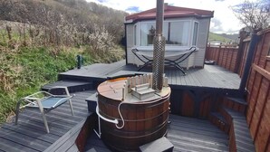 Una terraza con un barril de madera, una mesita y una silla. Se ve un edificio con techo rojo al fondo.