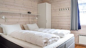 Une chambre à coucher avec un lit, une armoire, une étagère avec une lampe et une fenêtre avec des rideaux.