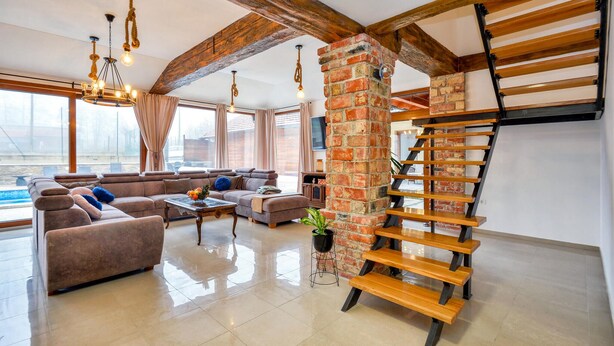 Een ruime woonkamer met een moderne zithoek, een houten trap en een groot raam met uitzicht op de omgeving.