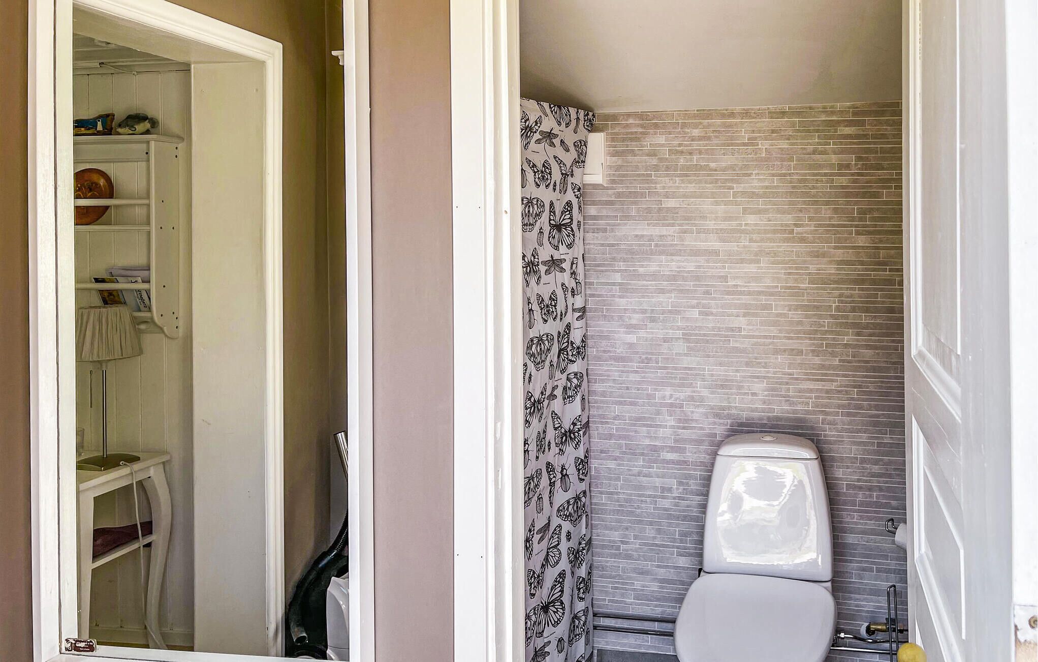 A bathroom with a toilet, a shower curtain with a butterfly pattern, and a brick wall.