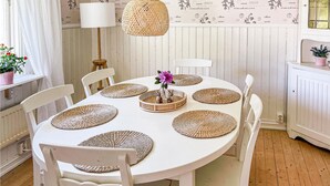 A round dining table with white chairs, surrounded by woven placemats, a vase with flowers, and a hanging woven light fixture. - Nice Home in Strömstad With 1 Bedrooms and Wifi (Stromstad)