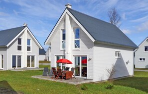 A modern two-story house with a patio area featuring a table and chairs, and a red umbrella. - Avendsünn (Kappeln)