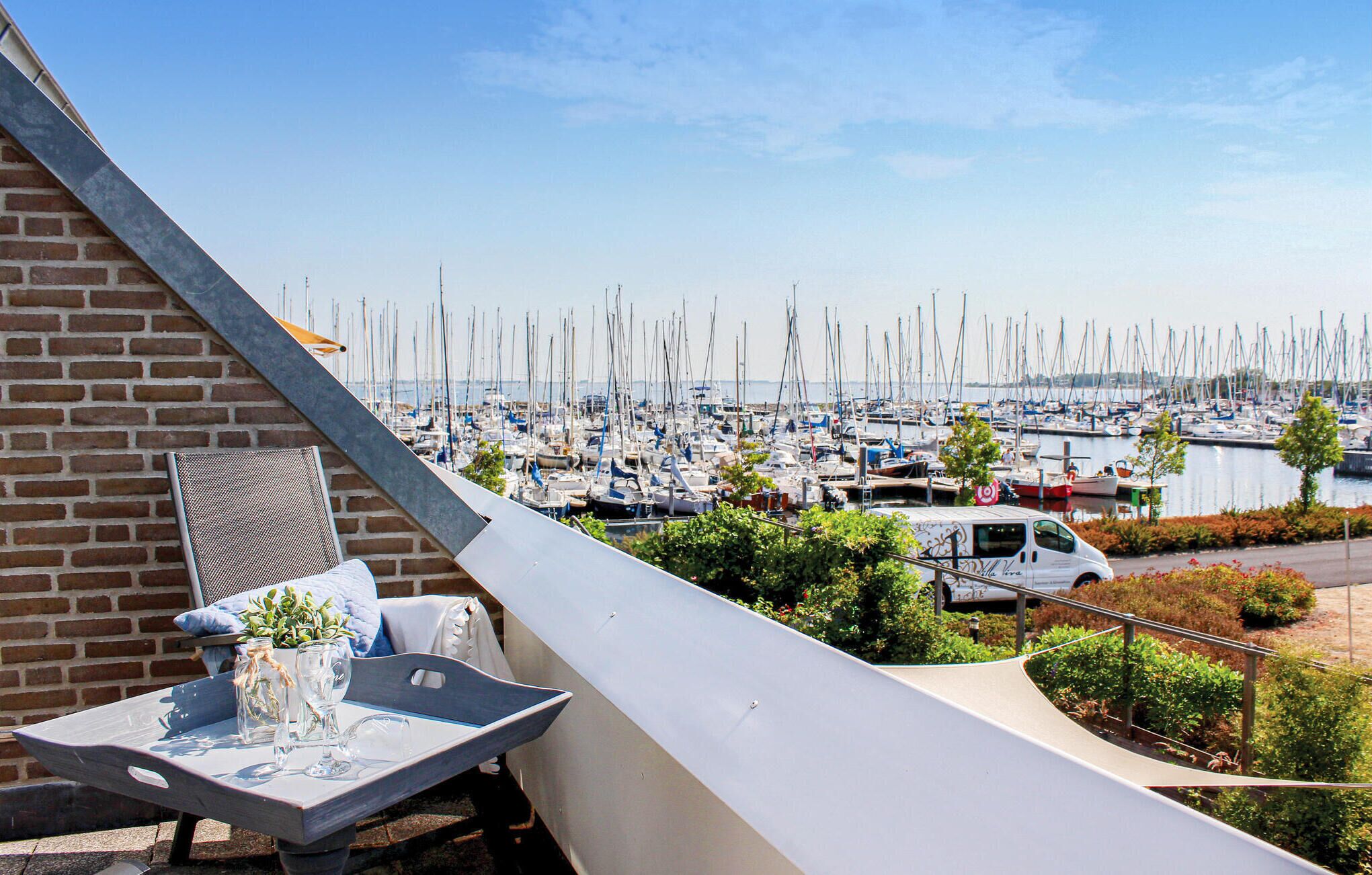 A balcony with a table, a white van, and a marina with numerous boats in the background.