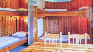 Eine Holzhütte mit Stockbetten, einem Holzesstisch und einer Wandleuchte.