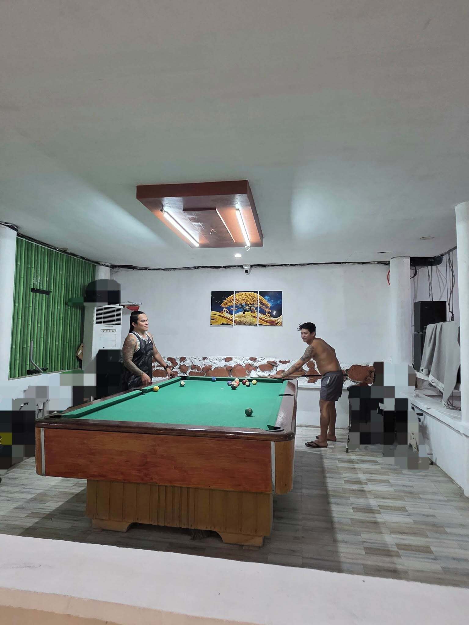 A pool table in a room with a green wall, a painting, and a ceiling light fixture.