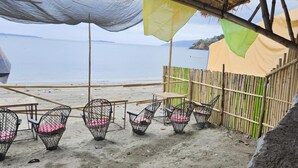 Un espace aménagé avec des chaises en osier et une structure à toit de chaume, situé au bord de la plage.