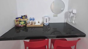 Une petite pièce avec une table noire, deux chaises rouges, une bouilloire, un miroir, un sèche-cheveux et des collations sur la table.