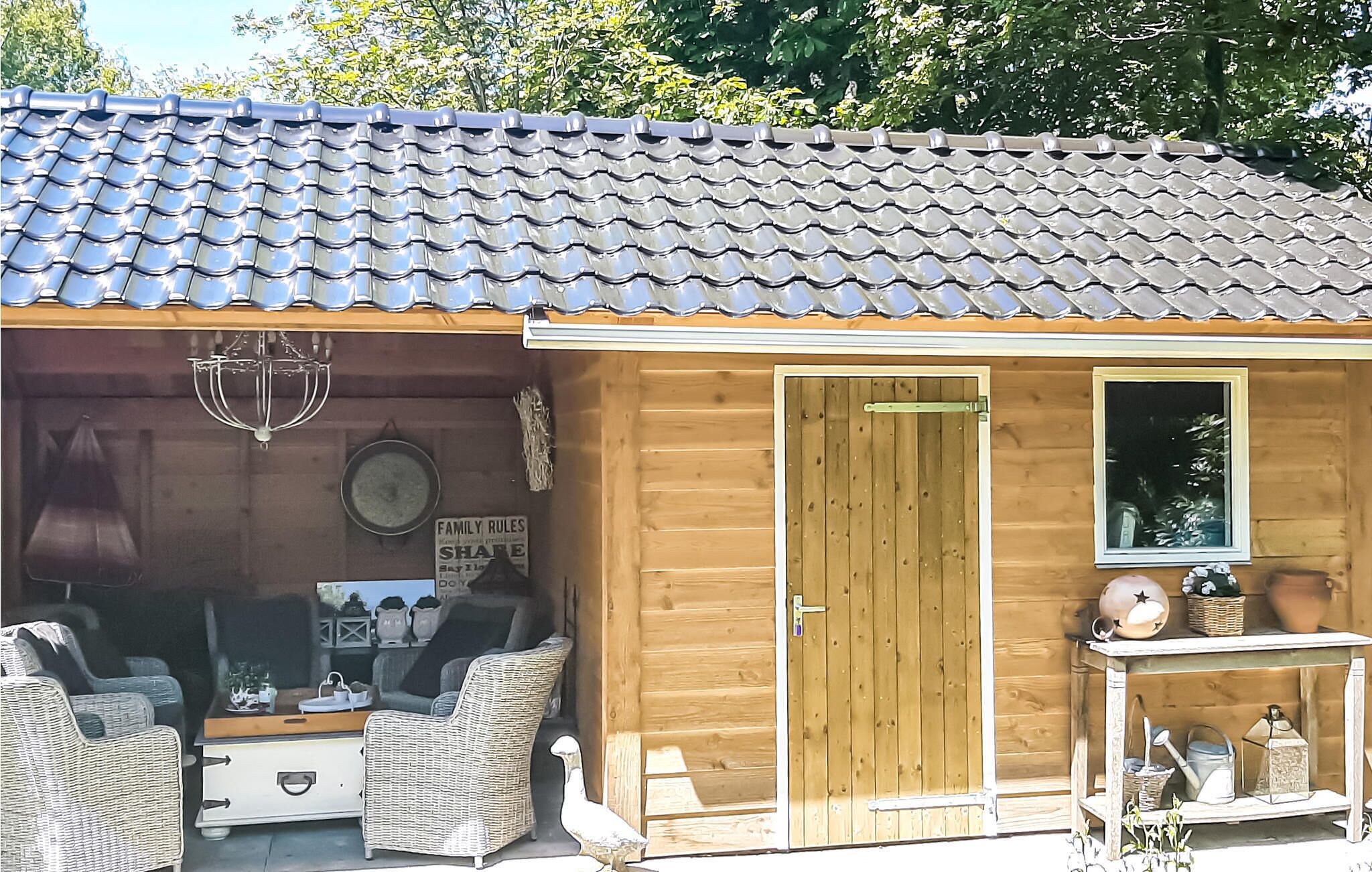 A wooden cabin with a tiled roof, a door, and a small porch area with wicker furniture and a table.