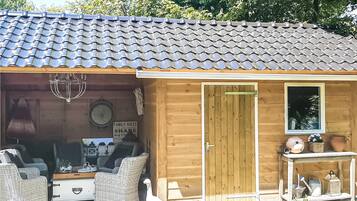 A wooden cabin with a tiled roof, a door, and a small porch area with wicker furniture and a table.