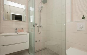 Un baño moderno con ducha de vidrio, un lavamanos blanco y dos dispensadores de jabón rosa, y un inodoro.